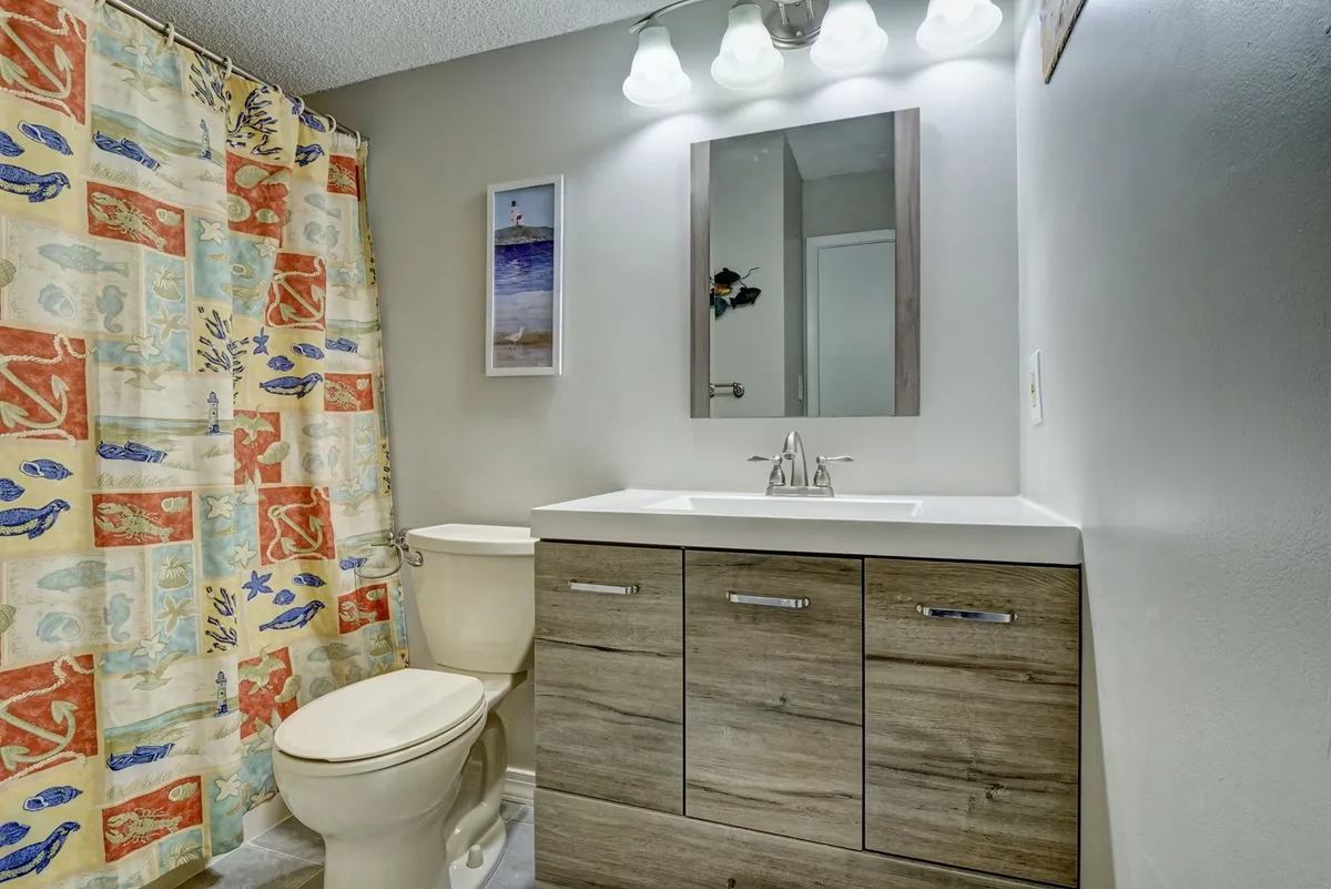 A fresh, modern bathroom with a colorful shower curtain, sleek vanity, and a well-lit mirror. The space feels inviting and clean, ideal for relaxing or getting ready for the day.