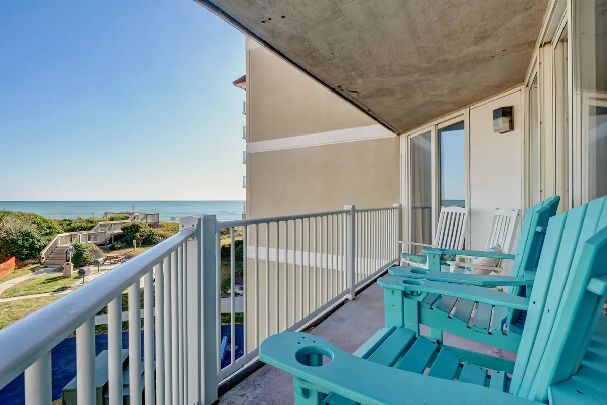 A tranquil balcony scene featuring turquoise Adirondack chairs positioned to face an expansive Atlantic Ocean view beyond a simple balcony railing. The calm, open water and horizon set a peaceful mood for quiet mornings or romantic sunset moments.
