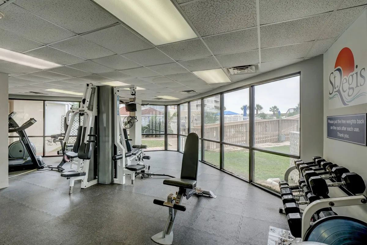 This image features the well-equipped fitness center, complete with modern exercise machines, large windows letting in natural light, and a range of free weights. Motivational signage on the wall and a spacious layout create an inviting atmosphere for wellness routines.