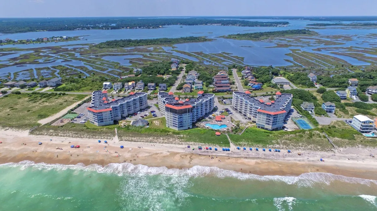 A lively beachfront property featuring a swimming pool with colorful umbrellas, sunbathers, and direct access to the sandy beach and the Atlantic Ocean. The energetic yet relaxed vibe invites guests to enjoy both poolside and seaside adventures.