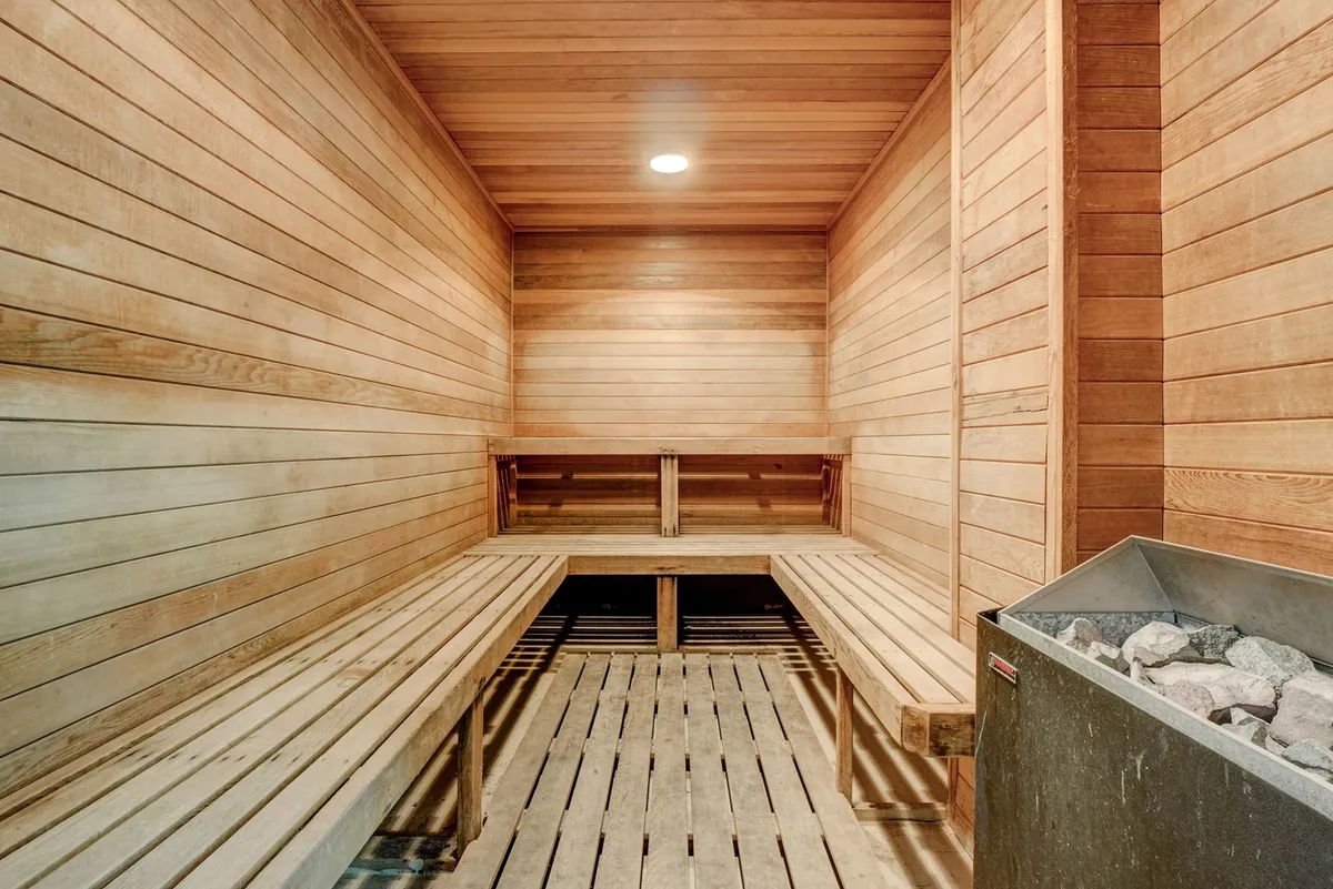 A calming sauna interior with wooden benches and a central stone heater, inviting guests to unwind after a busy day. The space is designed for relaxation and rejuvenation.